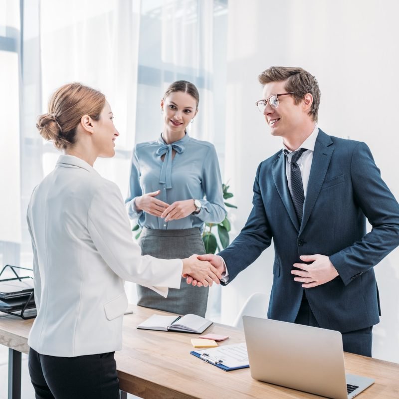 cheerful-recruiter-shaking-hands-with-woman-near-colleague-in-office.jpg